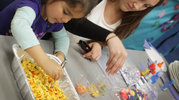 Young female child learning to sort colors using crackers with teacher