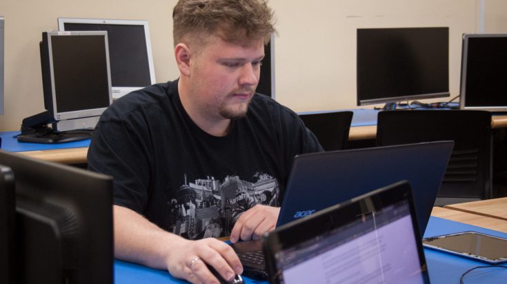 male student sitting at a computer in a computer lab classroom