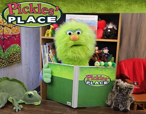 Green puppet holding a book titled Pickles Place
